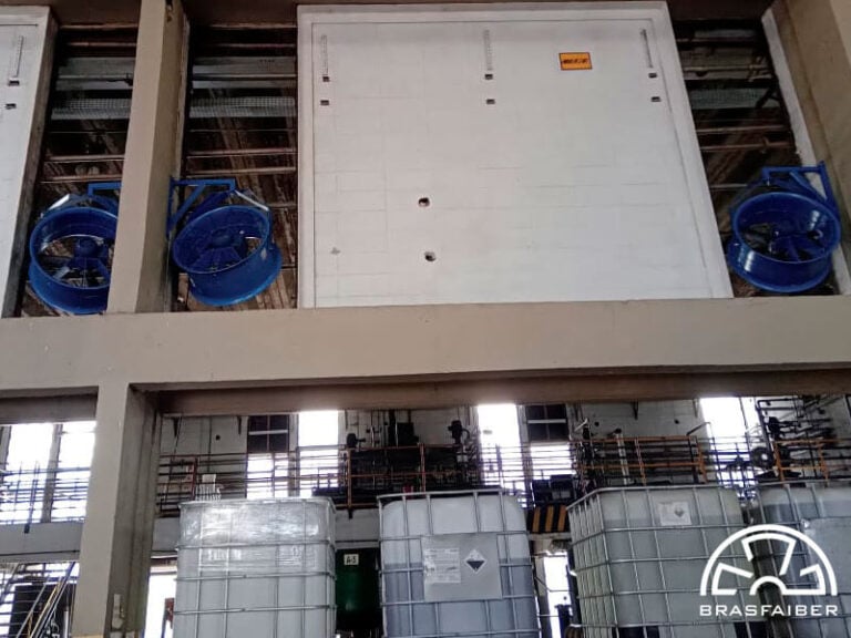 Ventiladores de parede insuflando ar sobre a área de trabalho de um galpão industrial